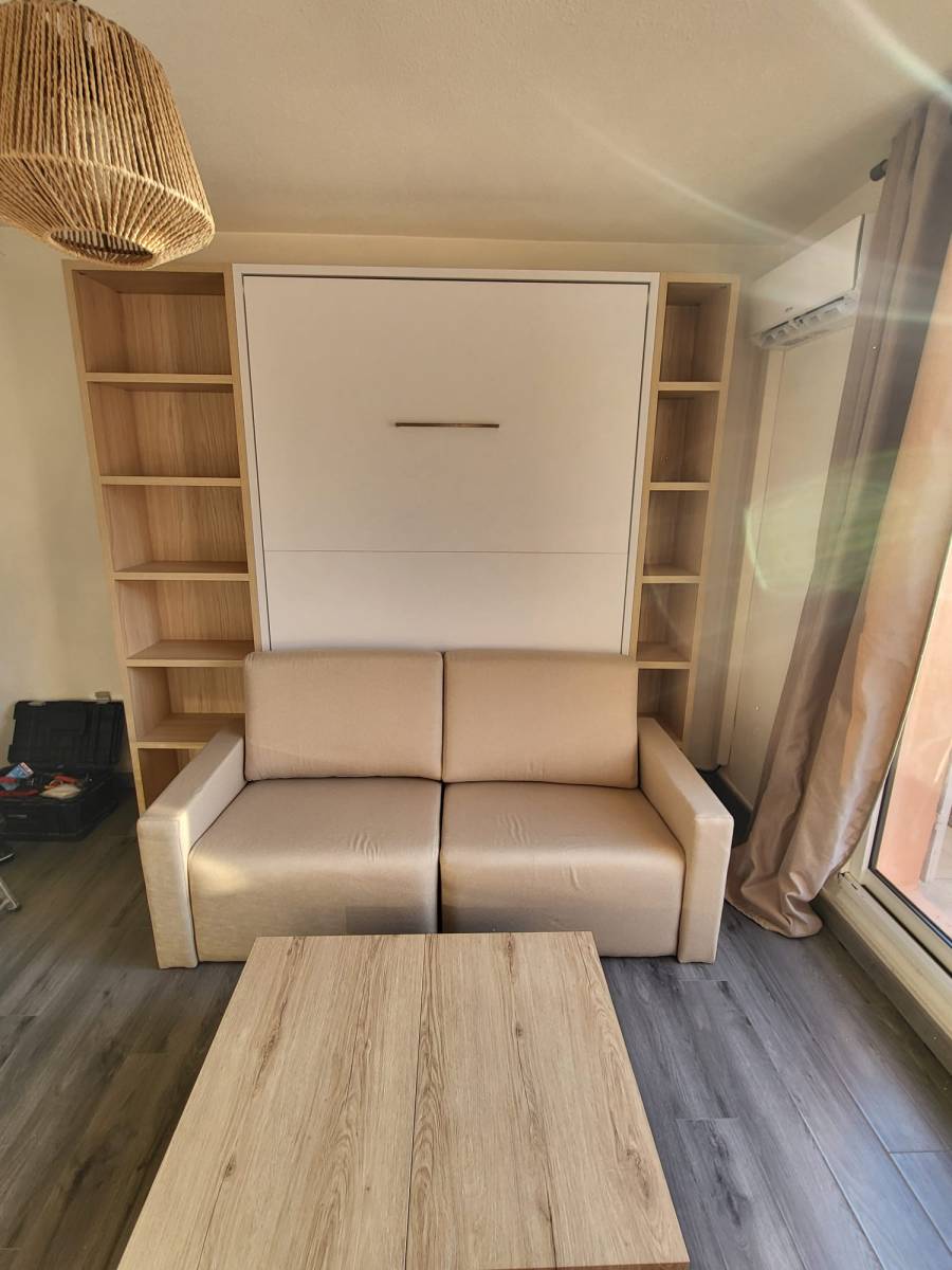 Aménagement gain de place composé d'un lit escamotable avec canapé, de 2 bibliothèques et d'une table basse transformable dans un studio proche de Bandol 